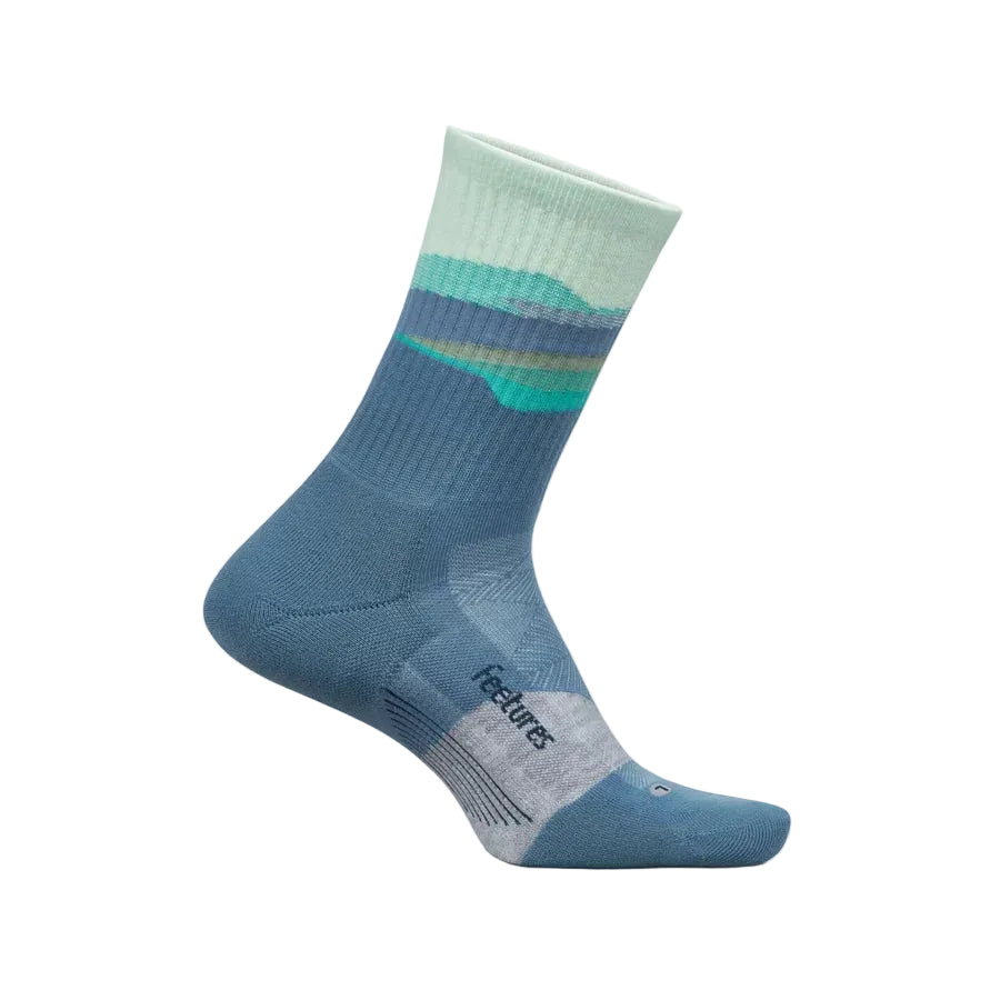 A single mid-calf sock in a dusty blue color with a striped mountain pattern in mint green, teal, and navy near the cuff, and a light gray textured toe cap. The brand name 'Features' is printed on the heel, shown against a light cream background.