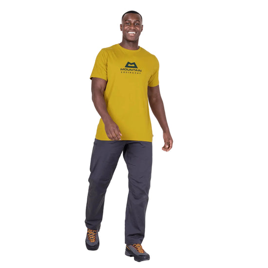 Man wearing a yellow t-shirt with a logo and gray pants on a white background