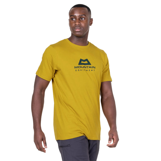 Man wearing a mustard yellow t-shirt with a logo on a white background