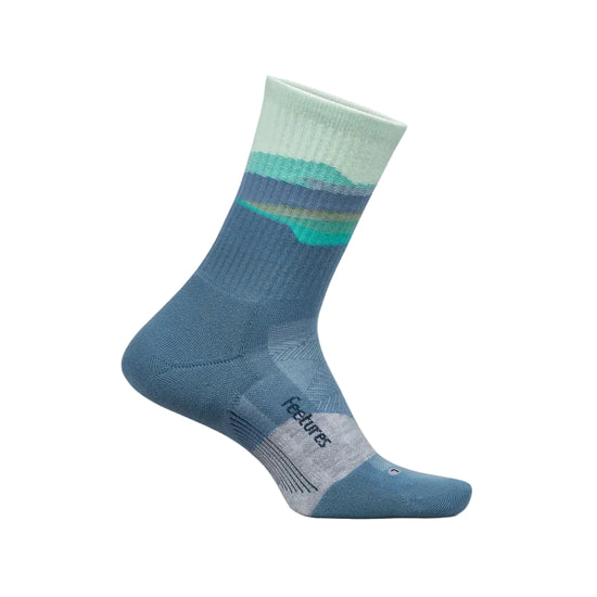 A single mid-calf sock in a dusty blue color with a striped mountain pattern in mint green, teal, and navy near the cuff, and a light gray textured toe cap. The brand name 'Features' is printed on the heel, shown against a light cream background.