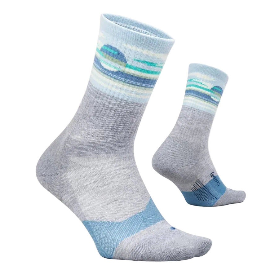 A pair of crew socks shown on invisible forms against a light cream background. The socks feature a heather gray body with a blue and teal wave pattern near the ribbed cuff, and a solid light blue toe section.