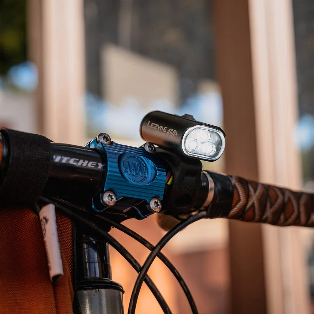 A close-up of a bicycle handlebar with a black LED front light mounted on a bright blue clamp.