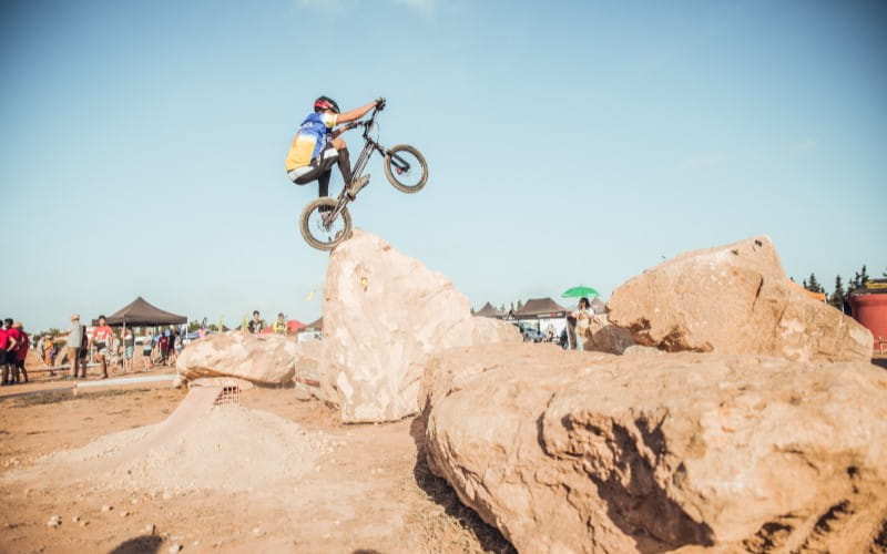 A trials rider leaps onto a large rock obstacle